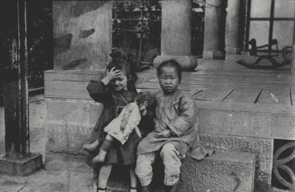 WHERE EAST MEETS WEST  Playfellows in Far Interior China. The little white girl is the daughter of a missionary in Suifu, Szech'uan, where picture was taken on porch of mission residence.