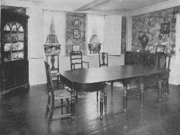 The warm tones of a brown Chinese wallpaper are  attractive with the mahogany furniture, and the pattern is prevented from becoming monotonous by the strong rectangular lines of the ivory woodwork which frames it. The corner cupboard and the exceptionally fine dining-table and the variety of chairs are interesting.