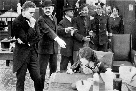 A man points at a scared woman. A demonically-grinning man is held by two policemen.