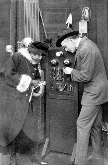 A man and a woman stand listening to a large radio.