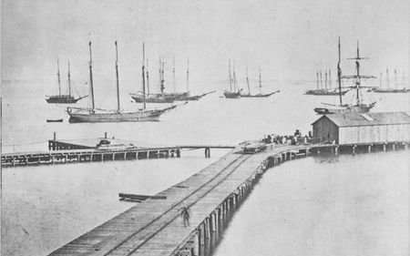 Schooners piled high with cartridge boxes lie in the placid waters off Hampton Roads. In 1865 hundreds of Union troops and supplies were moved by ocean transports, chartered at a daily cost of $92,000.