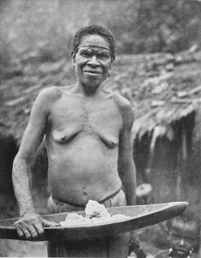 PAPUAN WOMAN CARRYING WOODEN BOWL OF SAGO.